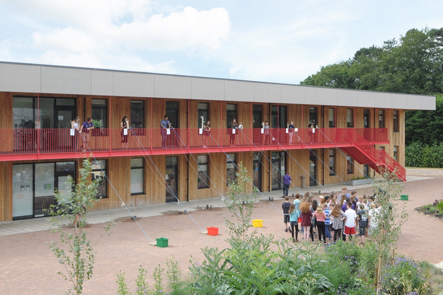 Kids standing and learning in front of a long building with windows in black frames